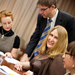 Photo of three people sitting at a table and one person standing at work.